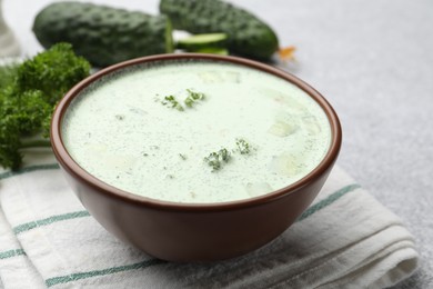 Photo of Tasty cucumber soup and ingredients on light grey table, closeup