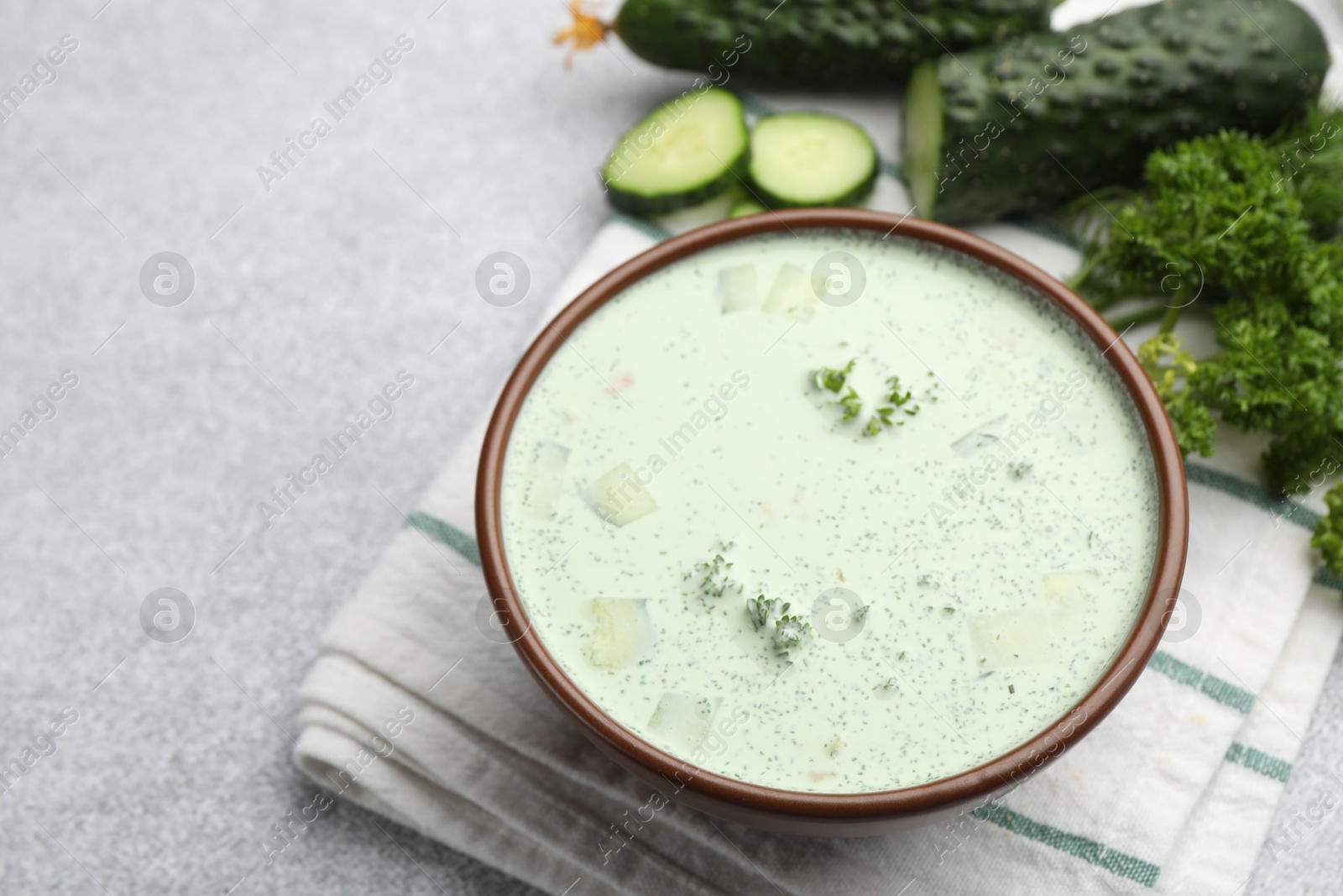 Photo of Tasty cucumber soup and ingredients on light grey table, closeup