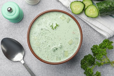 Photo of Tasty cucumber soup and ingredients on light grey table, flat lay