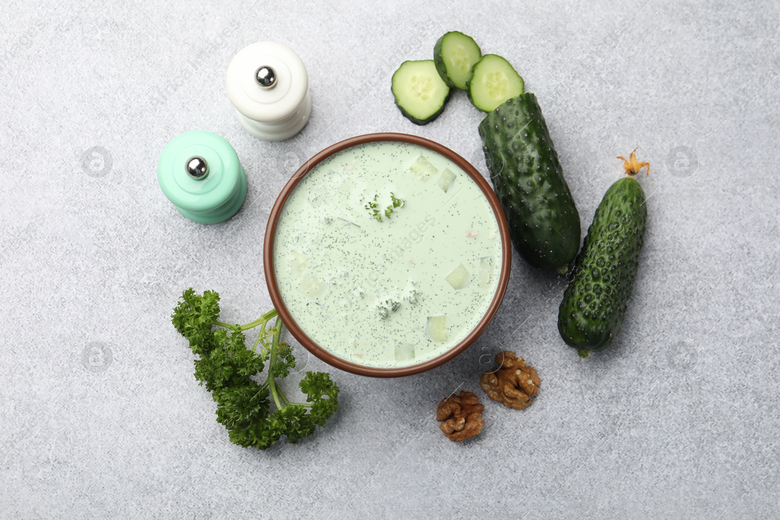 Photo of Tasty cucumber soup and ingredients on light grey table, flat lay