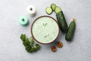 Photo of Tasty cucumber soup and ingredients on light grey table, flat lay