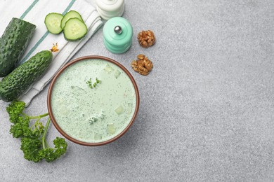 Photo of Tasty cucumber soup and ingredients on light grey table, flat lay. Space for text