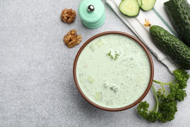 Photo of Tasty cucumber soup and ingredients on light grey table, flat lay. Space for text