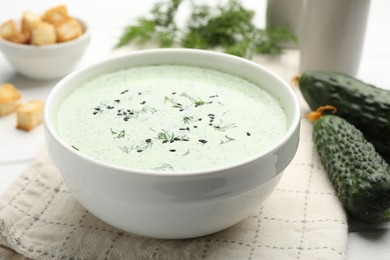 Photo of Tasty cucumber soup, croutons and ingredients on white wooden table, closeup