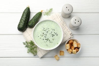 Photo of Tasty cucumber soup, croutons and ingredients on white wooden table, flat lay