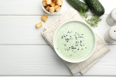 Photo of Tasty cucumber soup, croutons and ingredients on white wooden table, flat lay. Space for text