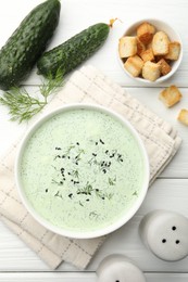 Photo of Tasty cucumber soup, croutons and ingredients on white wooden table, flat lay