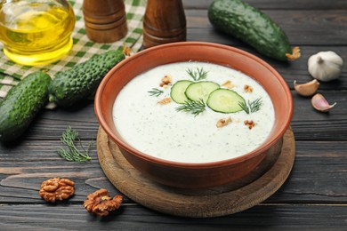 Photo of Tasty cucumber soup with dill, walnuts and ingredients on wooden table, closeup