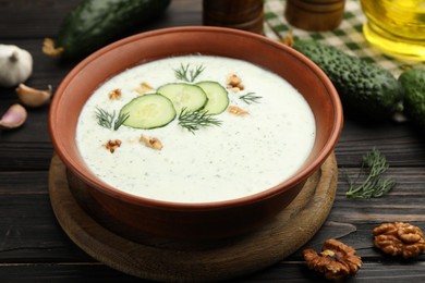 Photo of Tasty cucumber soup with dill, walnuts and ingredients on wooden table, closeup