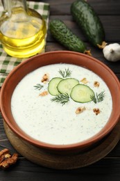 Photo of Tasty cucumber soup with dill, walnuts and ingredients on wooden table, closeup