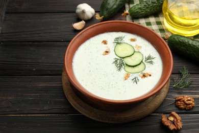 Photo of Tasty cucumber soup with dill, walnuts and ingredients on wooden table, closeup