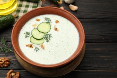 Photo of Tasty cucumber soup with dill, walnuts and ingredients on wooden table, closeup