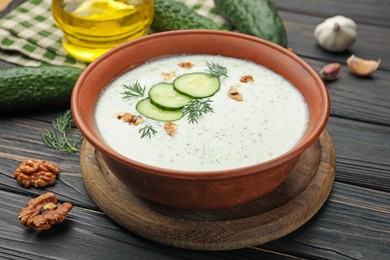 Photo of Tasty cucumber soup with dill, walnuts and ingredients on wooden table, closeup