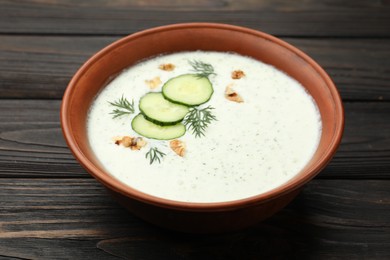 Photo of Tasty cucumber soup with dill and walnuts on wooden table, closeup