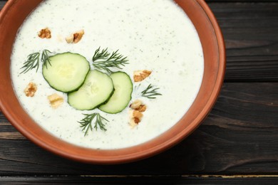 Photo of Tasty cucumber soup with dill and walnuts on wooden table, closeup