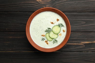 Photo of Tasty cucumber soup with dill and walnuts on wooden table, top view