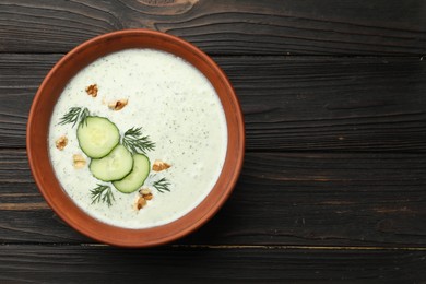 Photo of Tasty cucumber soup with dill and walnuts on wooden table, top view. Space for text
