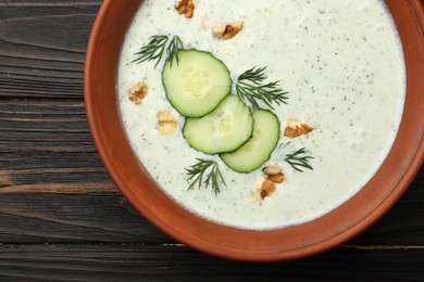 Photo of Tasty cucumber soup with dill and walnuts on wooden table, top view