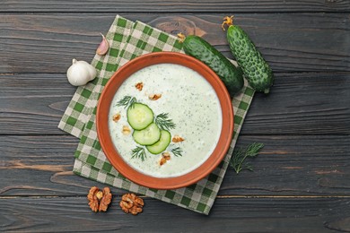 Photo of Tasty cucumber soup with dill, walnuts and ingredients on wooden table, flat lay