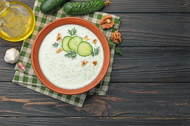 Photo of Tasty cucumber soup with dill, walnuts and ingredients on wooden table, flat lay. Space for text