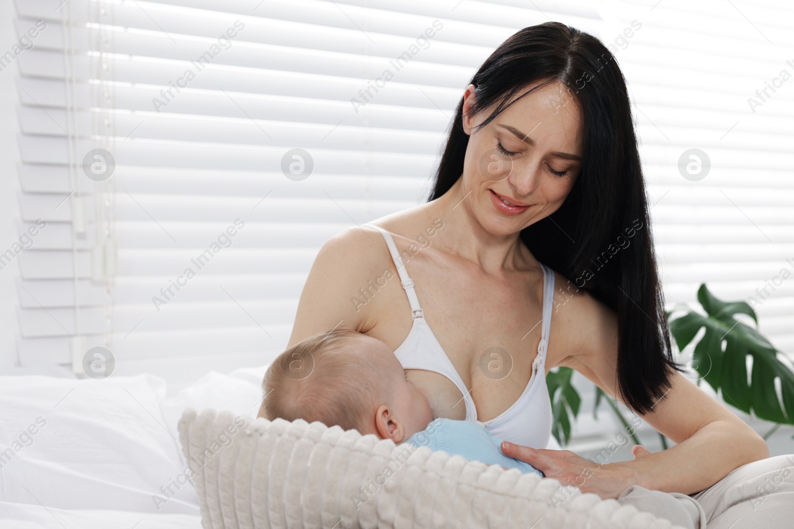 Smiling mother breastfeeding her little baby on bed at home Photo of Smiling mother breastfeeding her little baby on bed at home