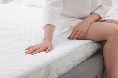 Photo of Woman touching soft mattress on bed indoors, closeup