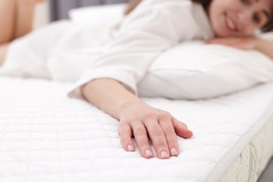 Photo of Woman touching soft mattress on bed indoors, selective focus