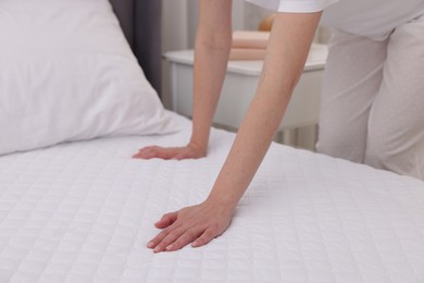 Photo of Woman touching soft mattress on bed indoors, closeup