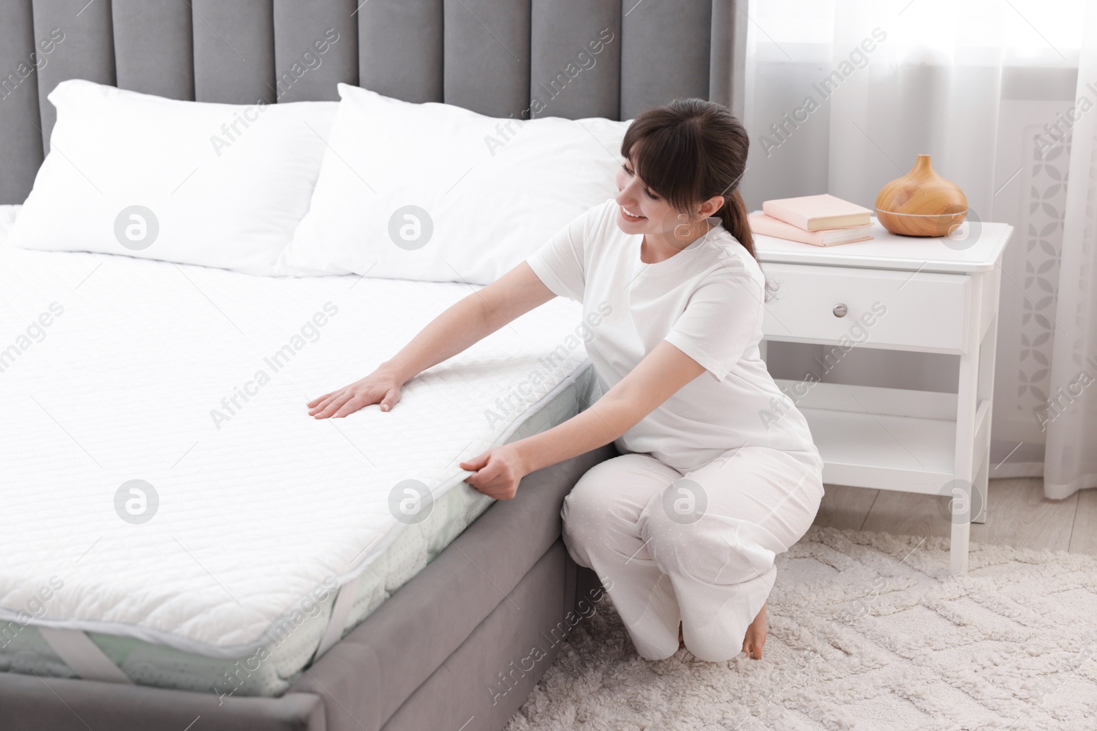 Beautiful woman putting cover on soft mattress at home Photo of Beautiful woman putting cover on soft mattress at home