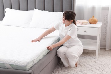Photo of Beautiful woman putting cover on soft mattress at home