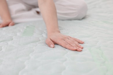Photo of Woman touching soft mattress on bed indoors, closeup