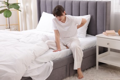 Photo of Woman suffering from back pain on bed at home