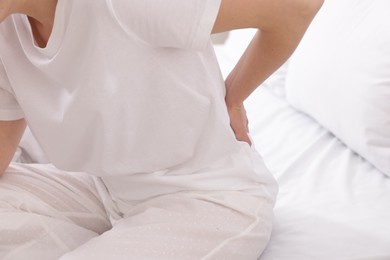 Photo of Woman suffering from back pain on bed, closeup