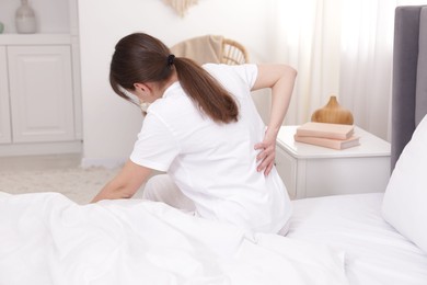 Photo of Woman suffering from back pain on bed at home