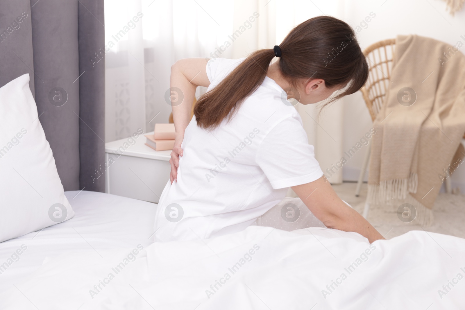 Photo of Woman suffering from back pain on bed at home
