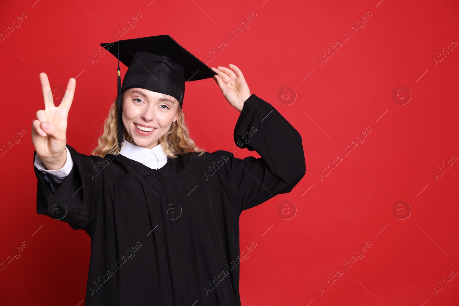 Happy student after graduation showing peace sign on red background. Space for text Photo of Happy student after graduation showing peace sign on red background. Space for text