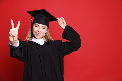 Photo of Happy student after graduation showing peace sign on red background. Space for text