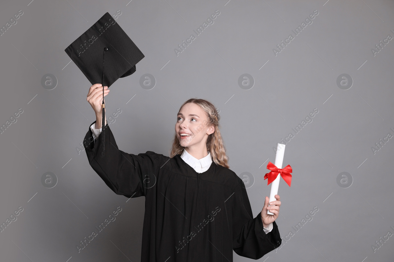 Happy student with diploma and mortarboard after graduation on grey background Photo of Happy student with diploma and mortarboard after graduation on grey background