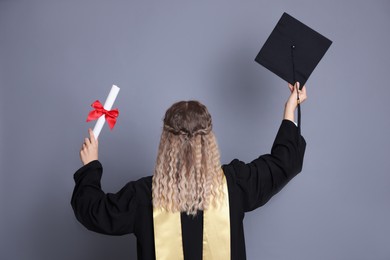 Photo of Student with diploma and mortarboard after graduation on grey background, back view