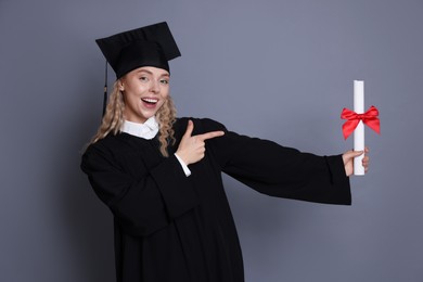Photo of Happy student pointing at diploma after graduation on grey background