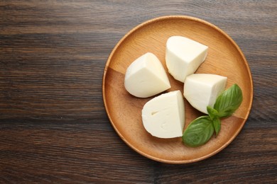 Photo of Pieces of delicious mozzarella cheese and basil on wooden table, top view. Space for text