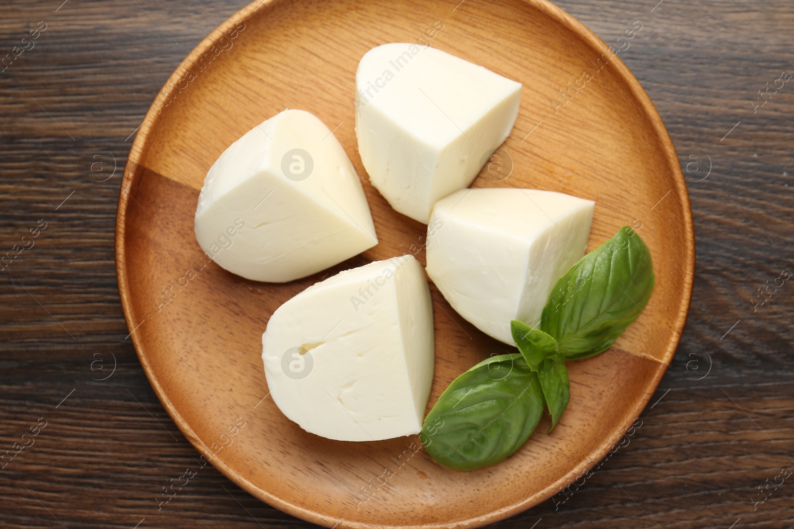 Pieces of delicious mozzarella cheese and basil on wooden table, top view Photo of Pieces of delicious mozzarella cheese and basil on wooden table, top view