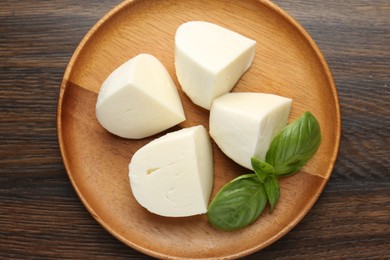 Photo of Pieces of delicious mozzarella cheese and basil on wooden table, top view
