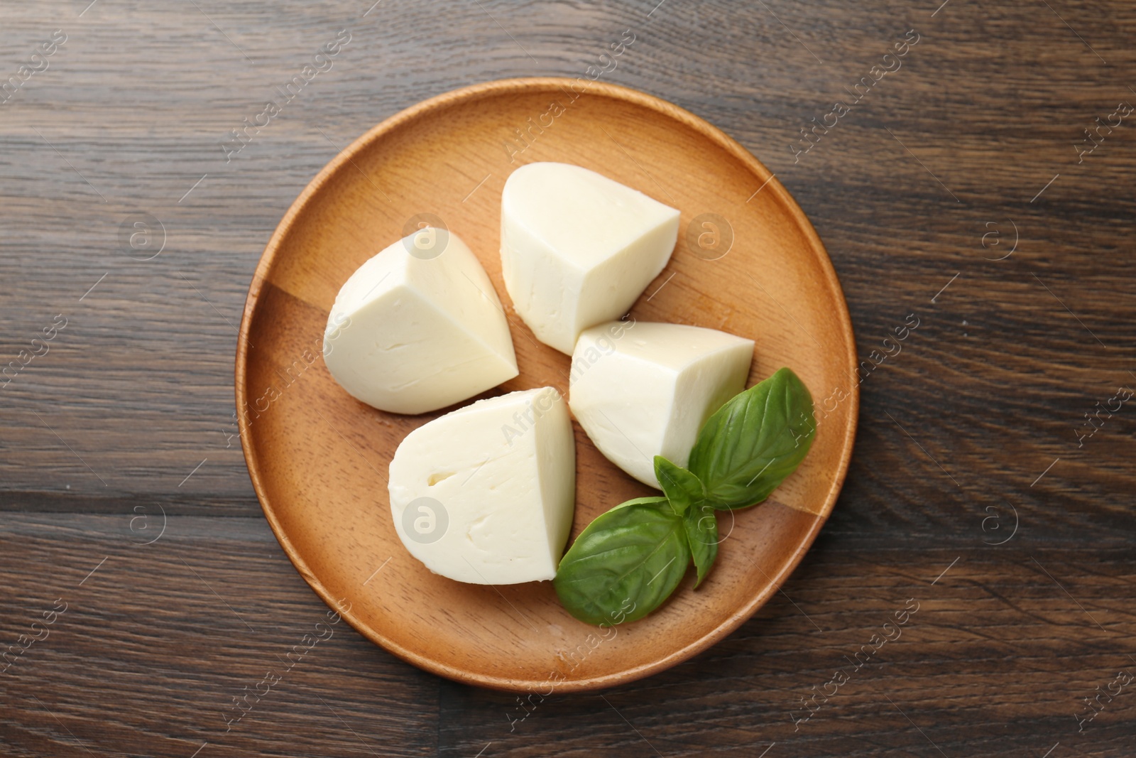 Photo of Pieces of delicious mozzarella cheese and basil on wooden table, top view