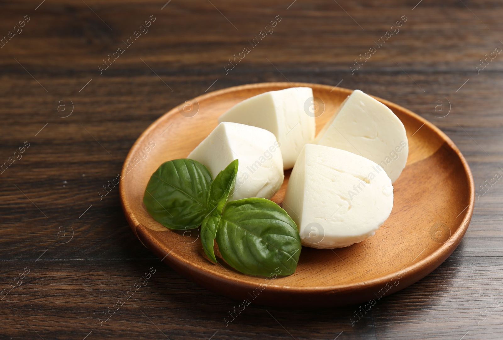 Pieces of delicious mozzarella cheese and basil on wooden table, closeup Photo of Pieces of delicious mozzarella cheese and basil on wooden table, closeup