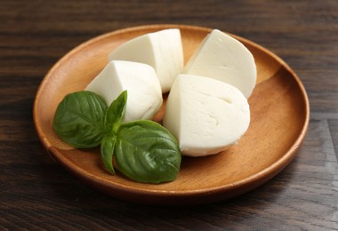 Photo of Pieces of delicious mozzarella cheese and basil on wooden table, closeup