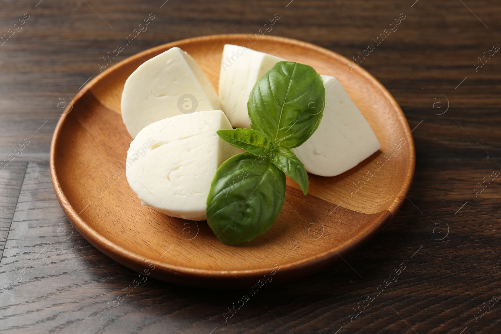 Pieces of delicious mozzarella cheese and basil on wooden table, closeup Photo of Pieces of delicious mozzarella cheese and basil on wooden table, closeup