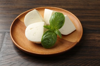 Photo of Pieces of delicious mozzarella cheese and basil on wooden table, closeup