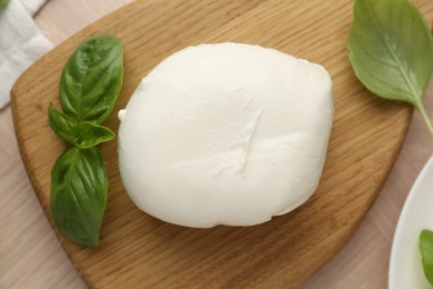 Photo of Piece of delicious mozzarella cheese and basil on wooden table, flat lay