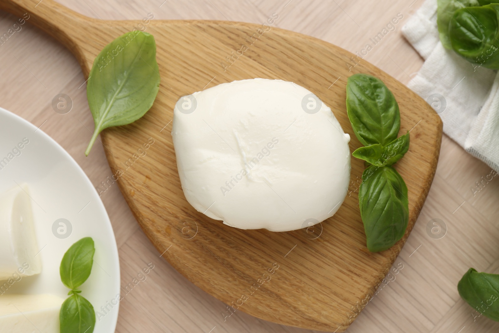 Piece of delicious mozzarella cheese and basil on wooden table, flat lay Photo of Piece of delicious mozzarella cheese and basil on wooden table, flat lay